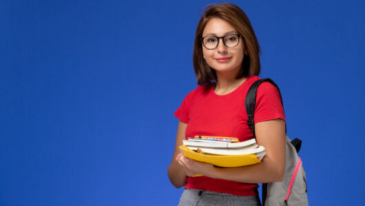 front-view-female-student-red-shirt-with-backpack-holding-books-files-smiling-blue-wall